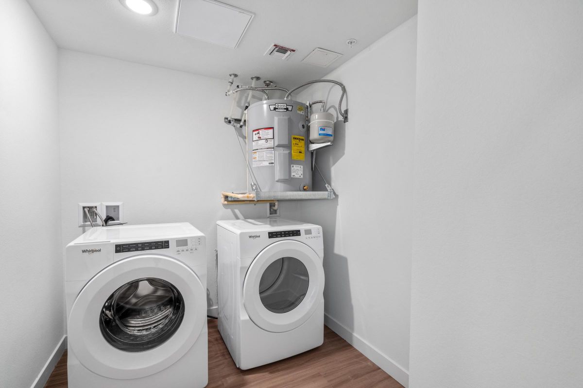 Laundry room with a washer, dryer, water heater, and bright white walls on a wood floor.