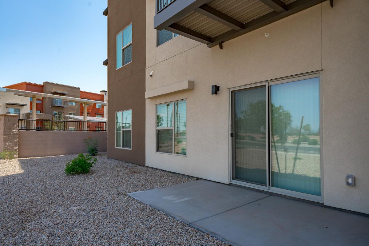Ground-floor apartment patio with sliding glass door, gravel yard, and a view of adjacent modern buildings.