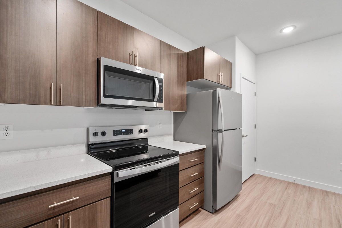 Modern kitchen with wood cabinets, stainless steel appliances, and light wood flooring.