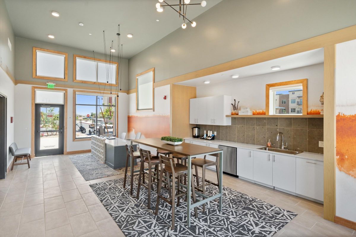Modern communal kitchen with high ceilings, tall windows, island seating, and neutral decor.