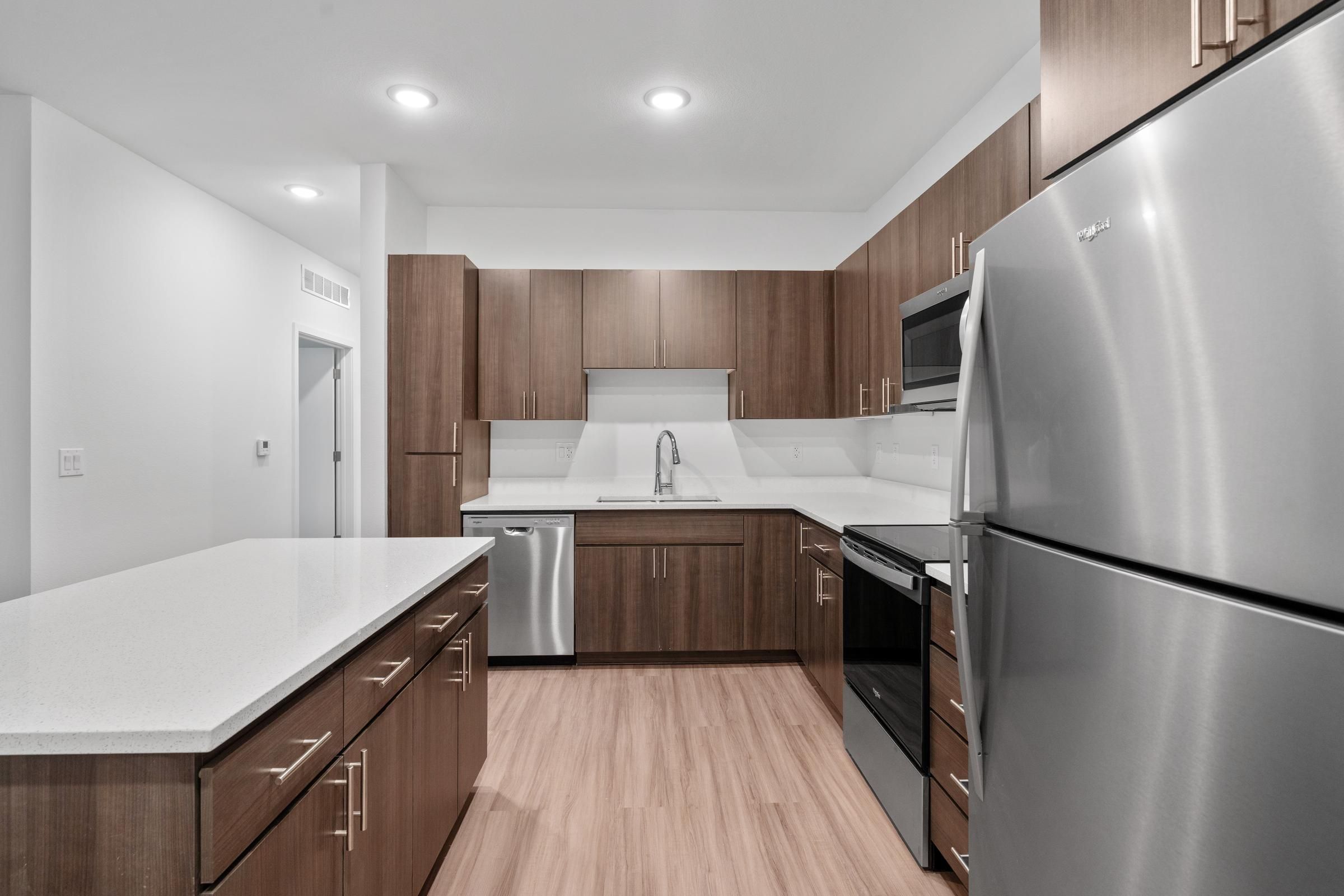 Modern kitchen with wood cabinets, stainless steel appliances, and a white countertop island.