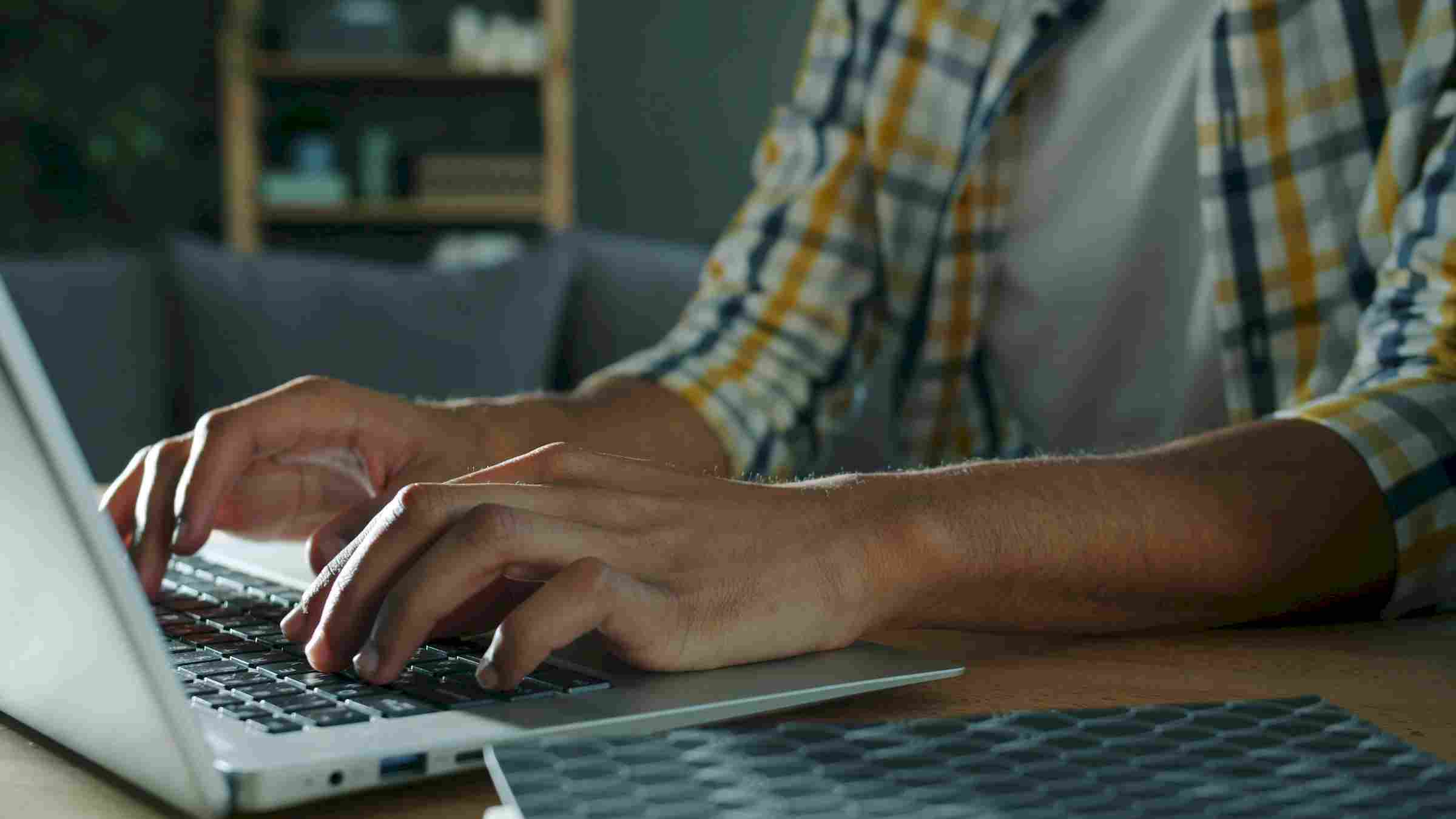 Affordable Apartments with Person typing on a laptop at a desk, wearing a plaid shirt, with a blurred background.